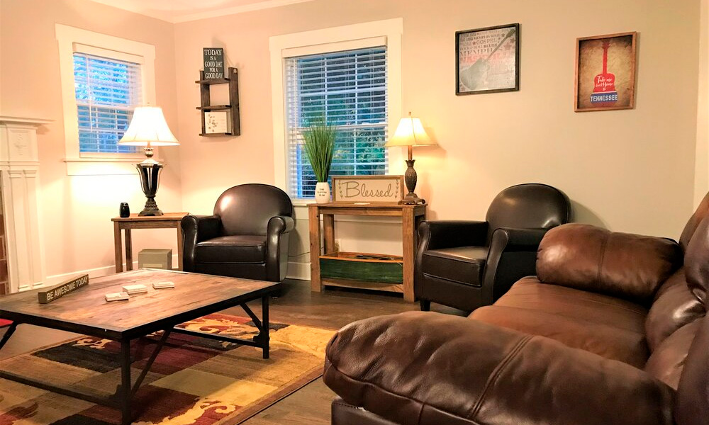 a living room area with two black single sofa, a large brown couch, laps, and a wooden center table over the carpeted flooring