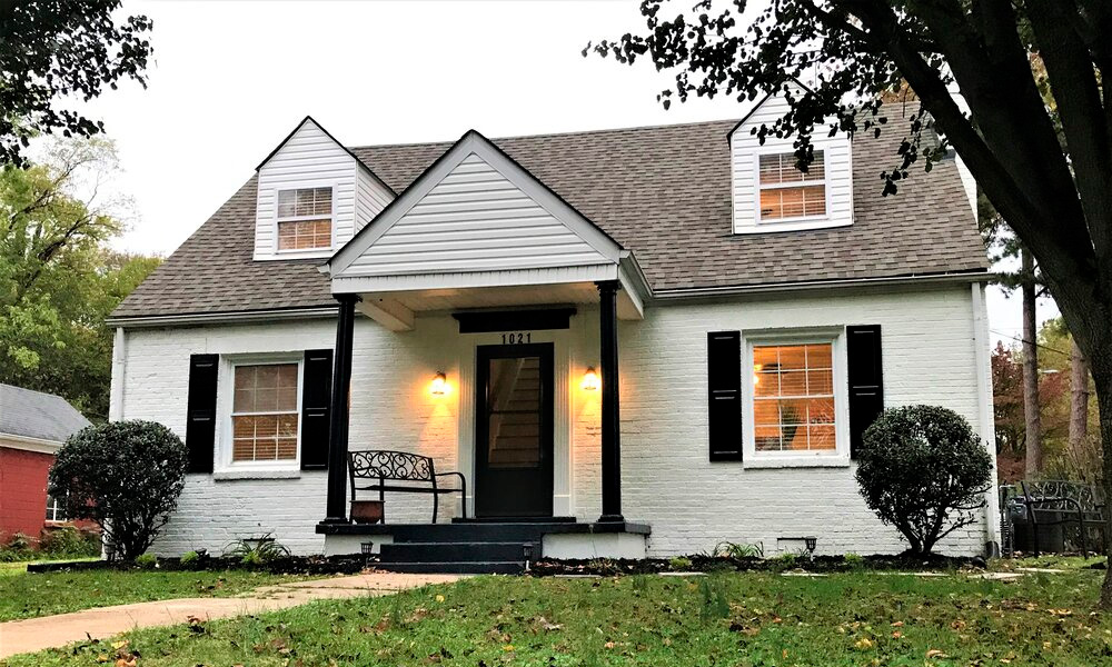 a house exterior with a porch, white walls, black detailed posts and windows, and a front yard